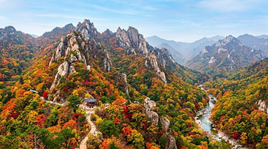 Pemandangan Pegunungan Seorak di Korea Selatan saat musim gugur, menampilkan tebing batu granit yang megah, pepohonan berdaun merah dan kuning keemasan di lembah.